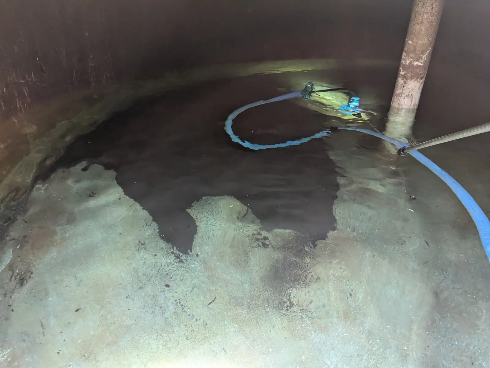 Half-cleaned tank floor — sludge on one side, bare concrete on the other